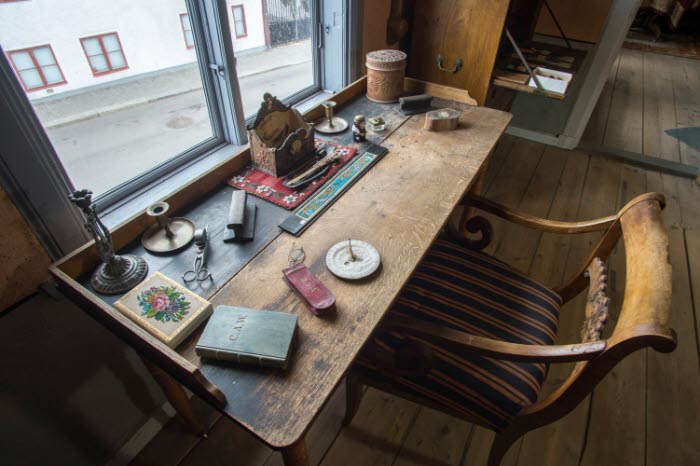 Interiör i museilägenheten i Onkel Adamsgården med bland annat ett skrivbord och en skrivbordsstol. Framför skrivbordet ett fönster med utsik mot huset på motstående sida av gatan.