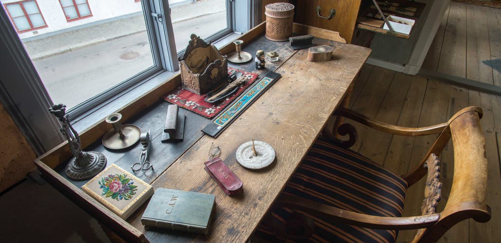 Interiör i museilägenheten i Onkel Adamsgården med bland annat ett skrivbord och en skrivbordsstol. Framför skrivbordet ett fönster med utsik mot huset på motstående sida av gatan.