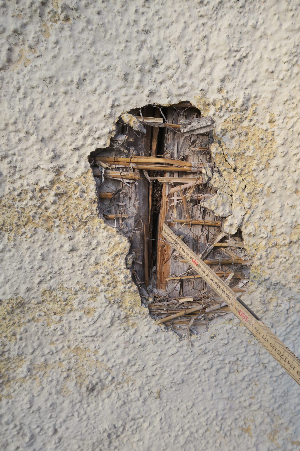 Detaljbild på en sprucken fasad genom vilken träpanelen syns igenom.
