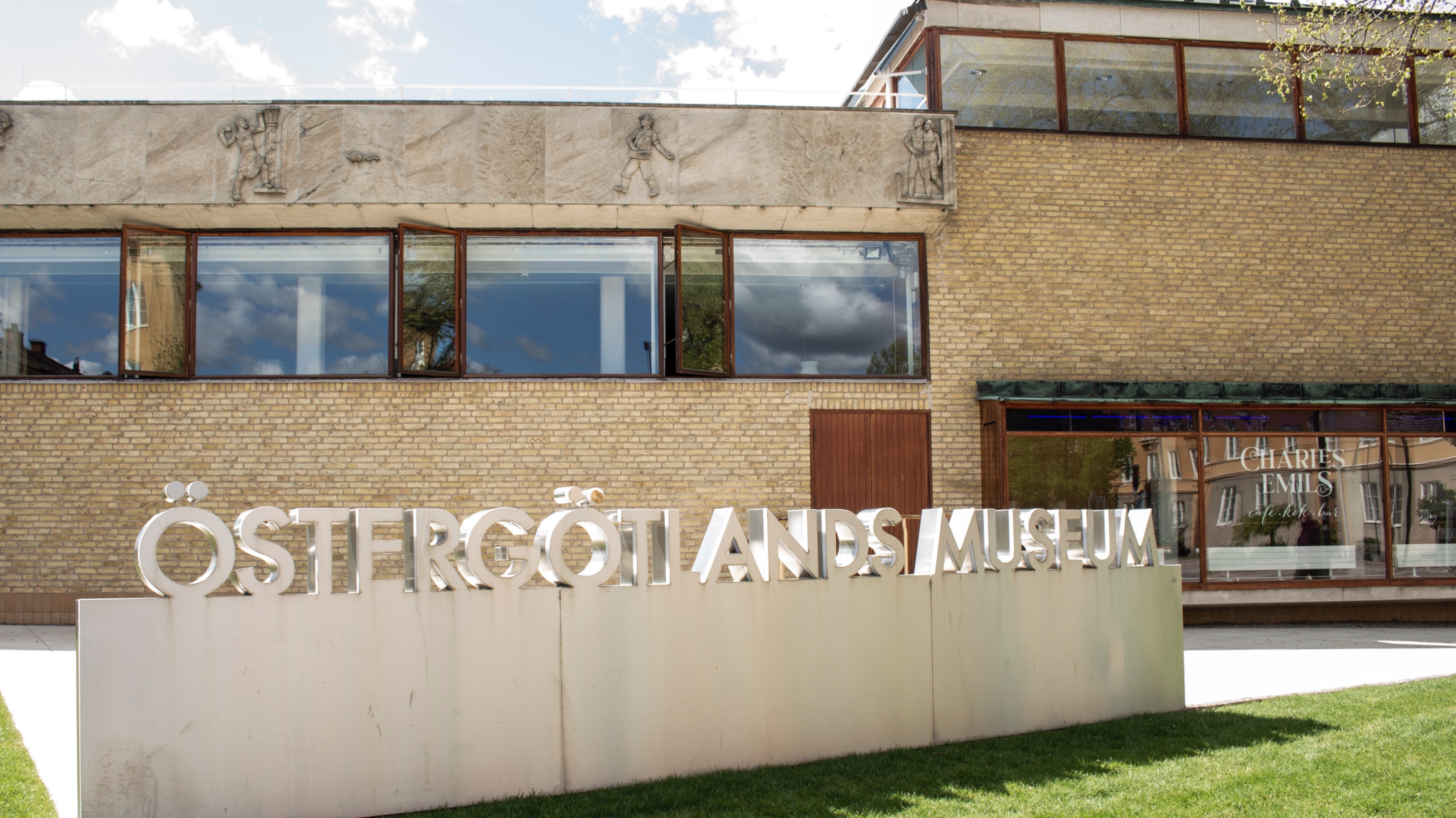 Gräsmatta och skylt "Östergötlands museum" framför museibyggnaden i Linköping.