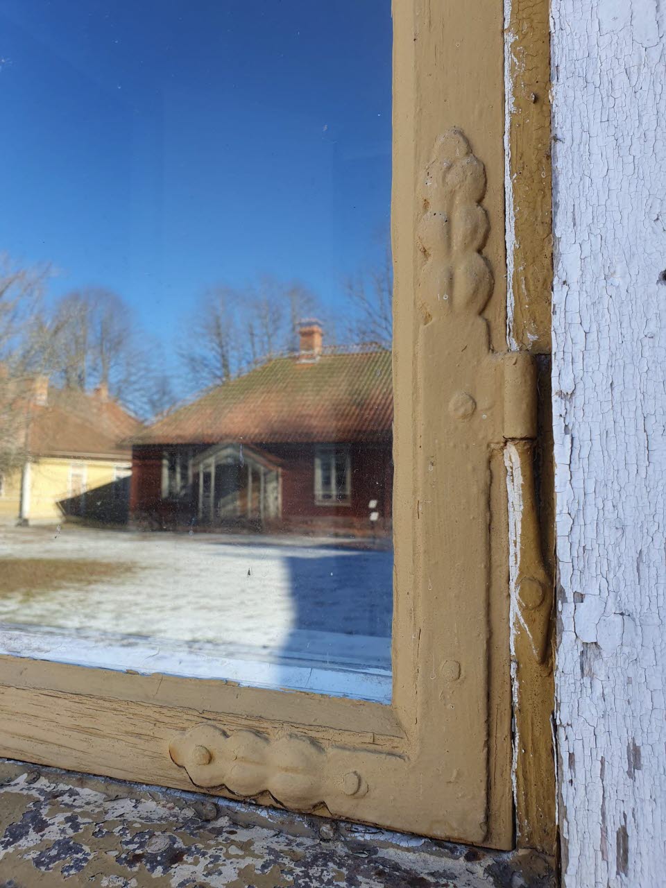 Ett äldre fönster i vilket det speglas ett rött torp.