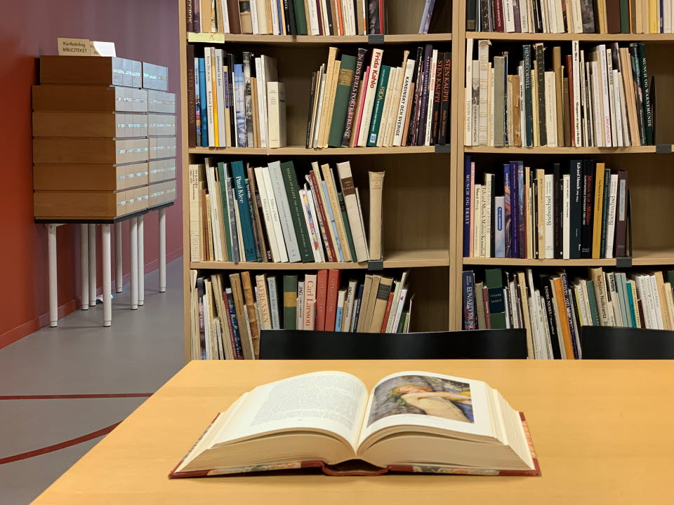 Museets bibliotek - uppslagen bok, hyllor och läsplats
