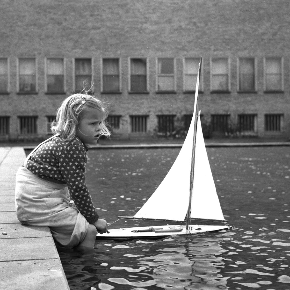 En flicka leker med en segelbåt i spegeldammen vid Östergötlands museum.
