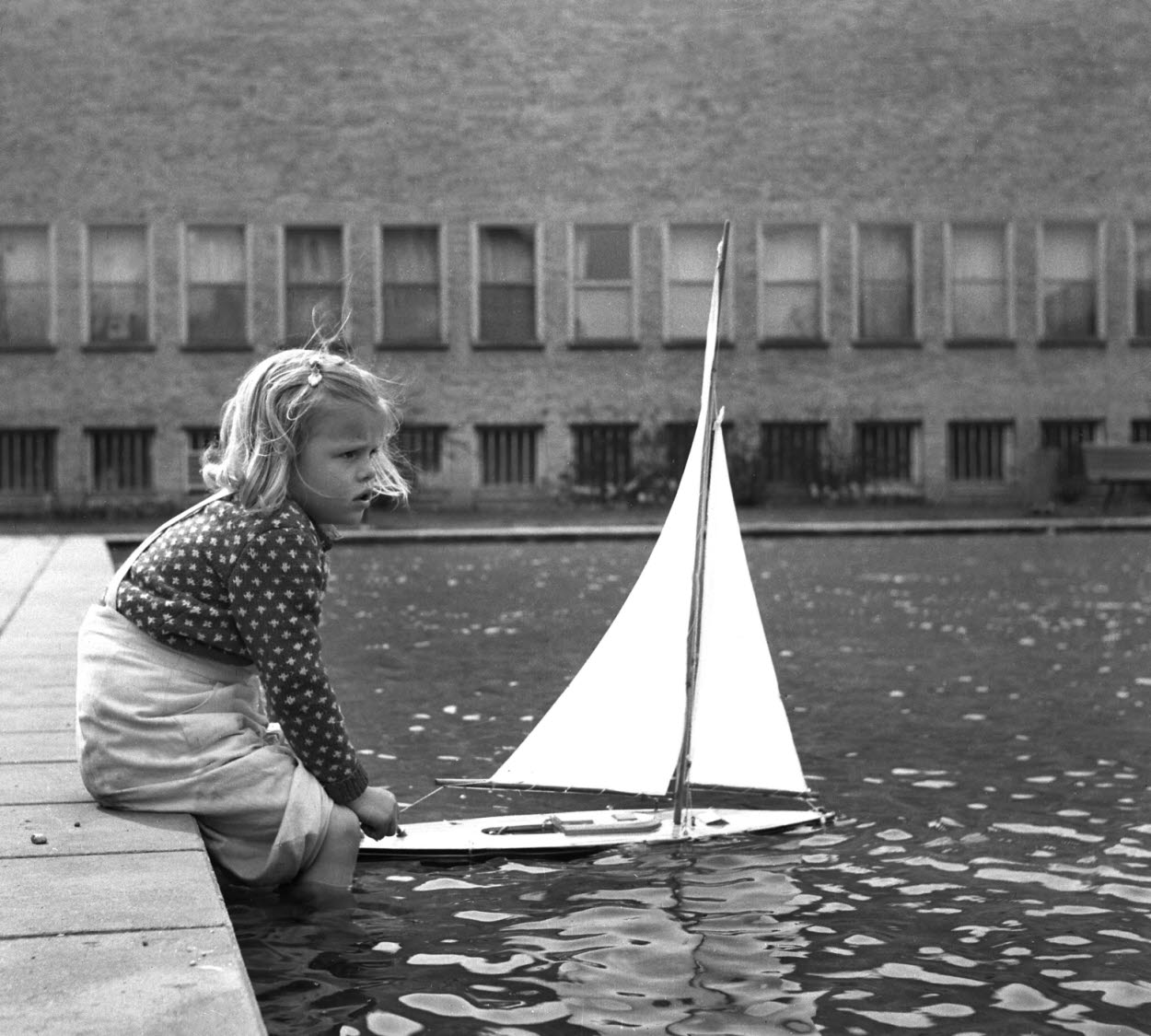 En flicka leker med en segelbåt i spegeldammen vid Östergötlands museum.