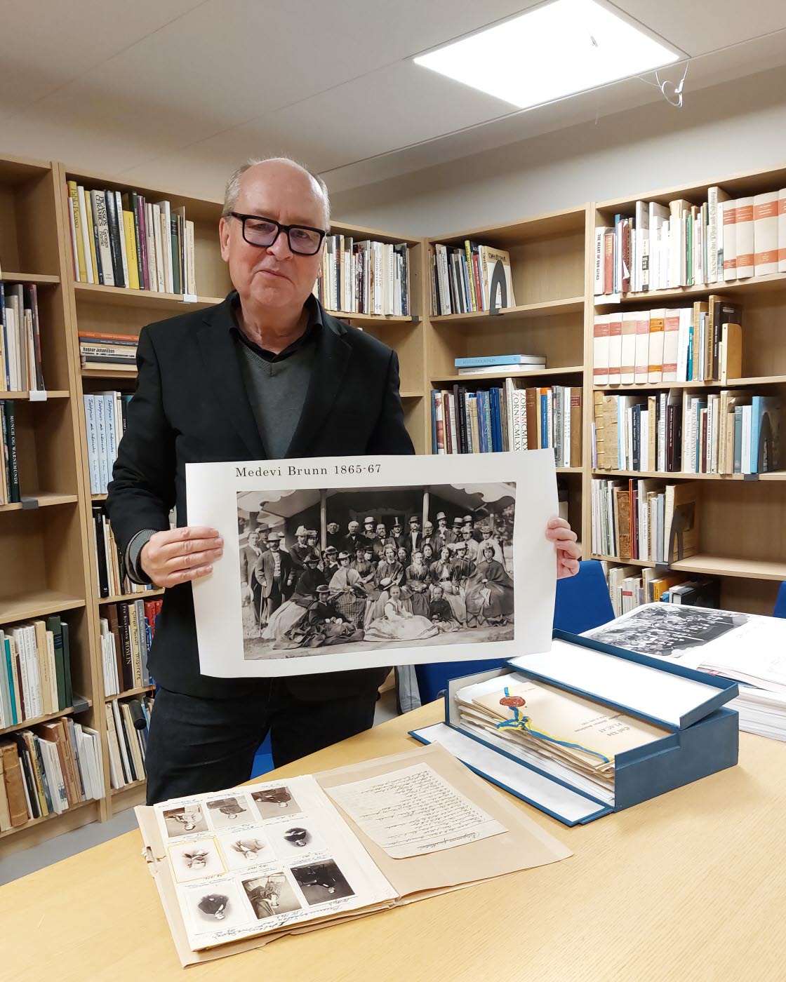 Arkivarie Jim Löfgren visar 1860-talsfotografier från Medevi brunn i Östergötlands museums arkiv och bibliotek.